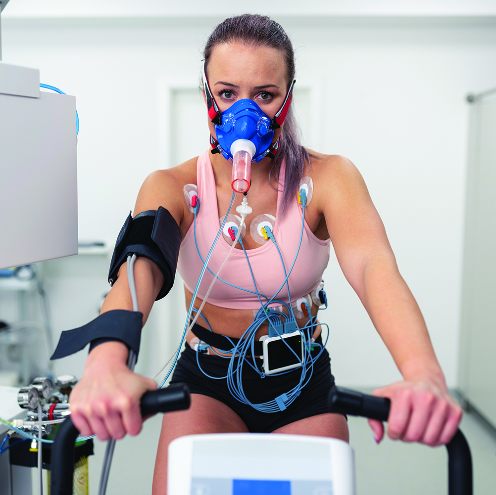Portrait of female athlete cycling on the ergometer and doing a cardiopulmonary test in clinic.