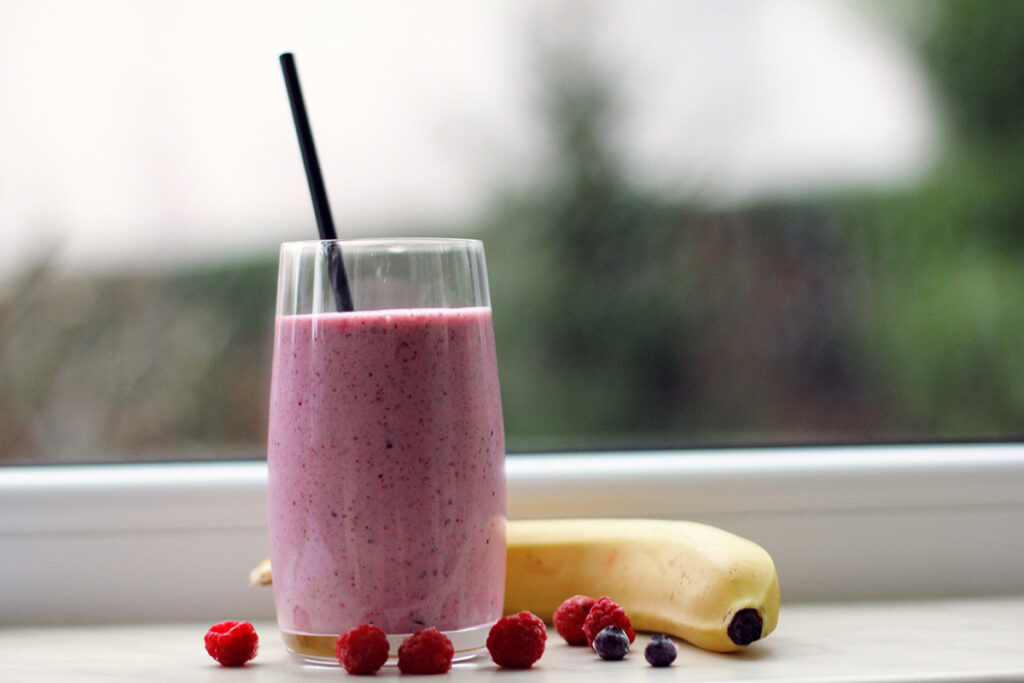 Fruit smoothie in a glass with berries and a banana on a table surrounding it